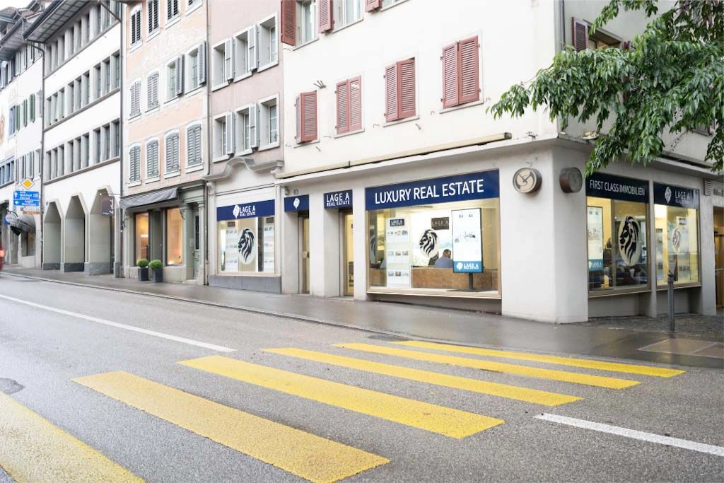 Aussenansicht des Büros von LAGE A Immobilien in Zug mit Schaufenstern und Schriftzug Luxury Real Estate